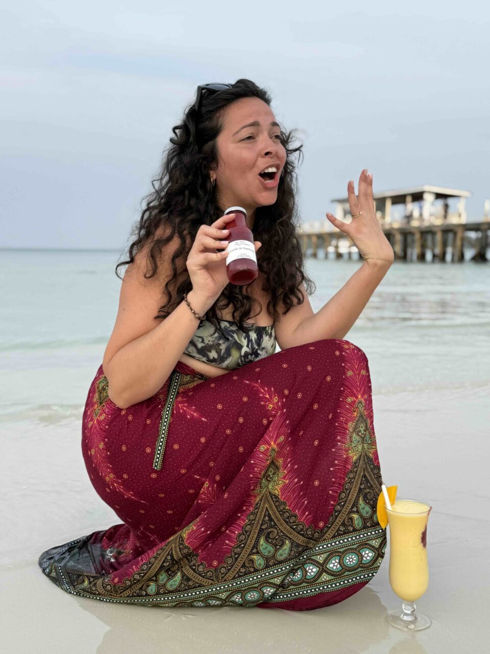 Jeune femme tenant du coulis sur la plage avec un verre de smoothie
