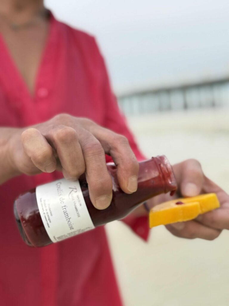 Main versant du coulis de framboise sur une mangue à la plage